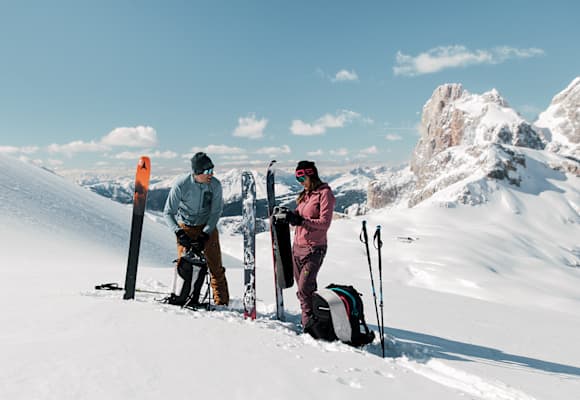Eine Frau und ein Mann stehen im Schnee auf einem Berg und machen sich für das Skifahren bereit.