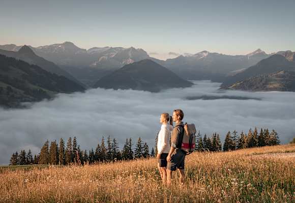 Zwei Wanderer genießen den Blick über ein Nebelmeer im herbstlichen Gstaad mit Bergpanorama im Hintergrund.
