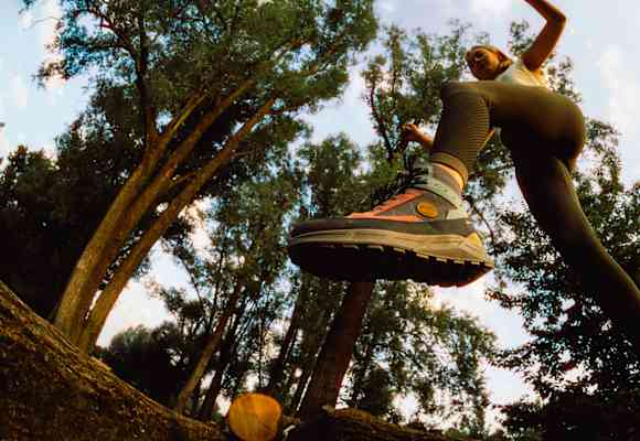 Frau springt im Wald über einen Baumstamm mit dem Hanwag Rotpunkt Light Mid GTX – leichter, vielseitiger Outdoor-Schuh für Alltag und Wanderungen