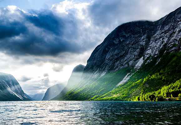 Norwegischer Fjord bei Sonnenaufgang mit schroffen Klippen und Wald 