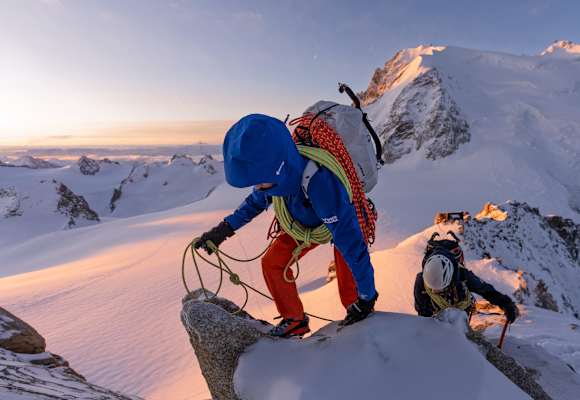 Ein Bergsteiger mit der neuen Mammut Eiger Extreme Kollektion klettert über einen verschneiten Felsgrat. Am kurzen Seil sichert er einen Nachsteiger, der mit einem Eispickel unterwegs ist.