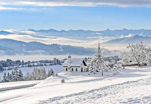 Die Hubertuskapelle in Scheidegg im Allgäu inmitten einer tief verschneiten Berglandschaft.
