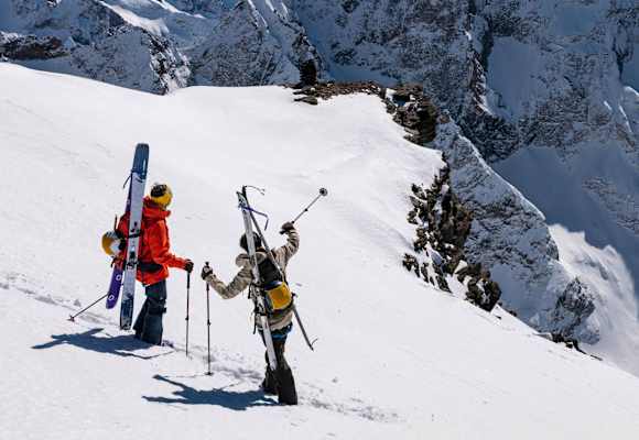Auf einem schneebedeckten Hang stehen zwei Skitourengeher und zeigen in die Ferne. Sie sind mit der Bergtagen-Kollektion von Fjällräven ausgerüstet.