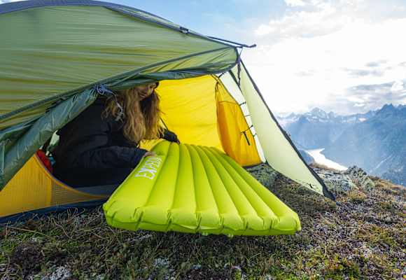 Eine Frau sitzt in einem Zelt und zieht eine Schlafmatte von Exped hinein.