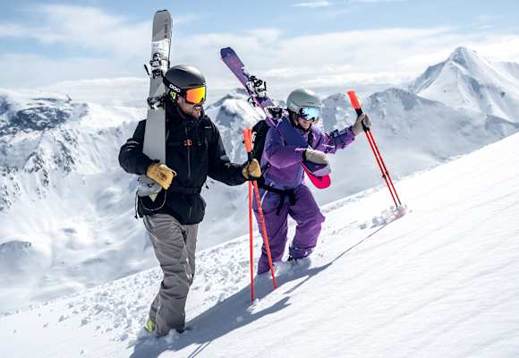 Ein Skifahrer und eine Skifahrerin gehen eine Piste in Ischgl hinauf.