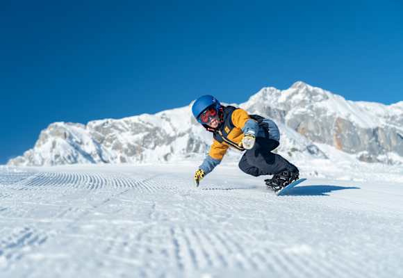 Ein Kind fährt in Snowboardbekleidung im Winter die Piste herunter.