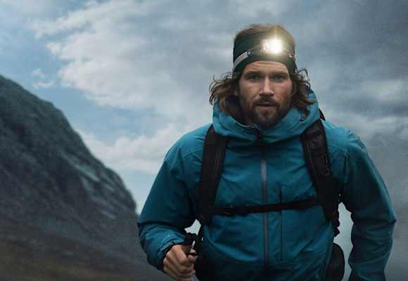 Ein Mann mit einer leuchten Stirnlampe geht mit Wanderausrüstung