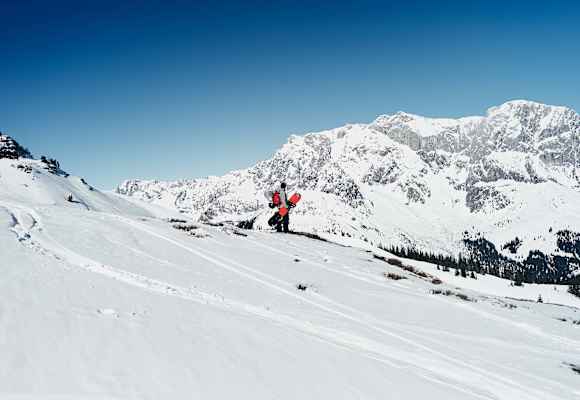 Ein Snowboarder steht in der Winterlandschaft mit Blick auf den Hochkönig.