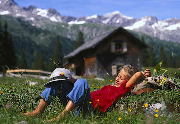 Mädchen auf einer Almwiese mit Berghütte im Hintergrund