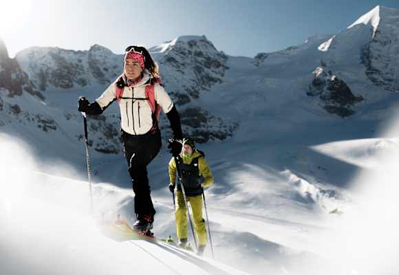 Skitourengeherin und Skitourengeher mit Dynafit-Ausrüstung beim Aufstieg im winterlichen Hochgebirge unter blauem Himmel.