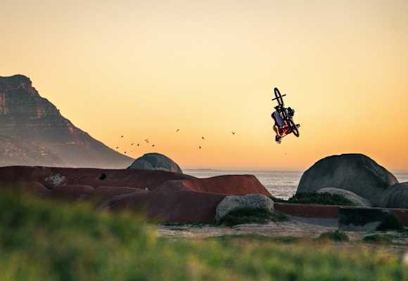 BMX-Biker dreht sich in Luft vor Küstenszenerie.