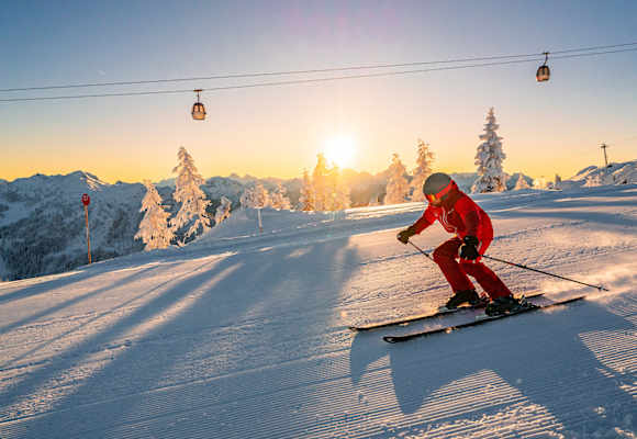 Skifahrer fährt den Berg hinunter bei Sonnenuntergang