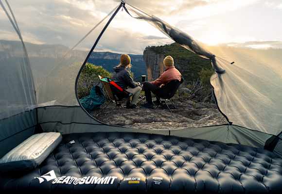 Sea to Summit Isomatte und Kissen im Zelt mit Blick auf zwei Camper, die den Sonnenuntergang in den Bergen genießen