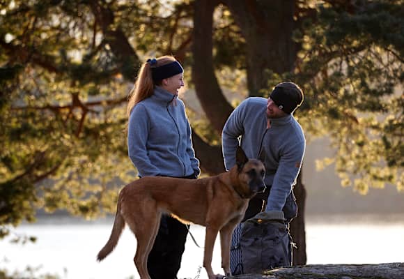 Ein Paar in Sportkleidung aus Merinowolle mit Schäferhund im Park im Herbst.