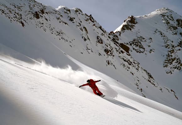 Eine Person fährt Snowboard im Schnee auf einem Berg in roter Ausrüstung.