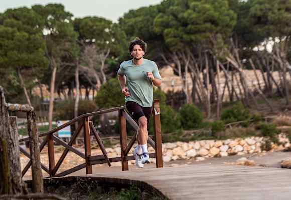 Ein Mann läuft im neuen Trailrunning-Outfit von skinfit über eine Brücke aus Holz.