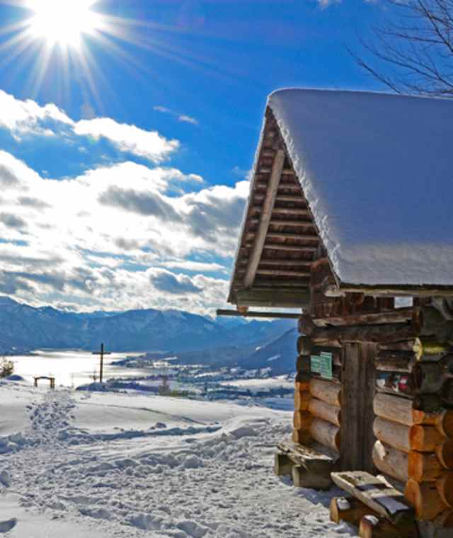Blockhütte mit Schneedache inmitten einer Winterlandschaft am Buchberg mit Blick zum Attersee, Salzkammergut.