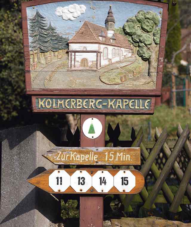 Holzgeschnitztes Schild auf dem Weg zur Kolmerberg-Kapelle.